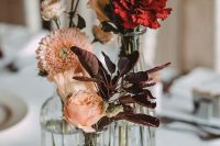 a cluster wedding centerpiece of vases with dark foliage, blush and red blooms is very lovely for fall