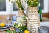a cluster wedding centerpiece of woven vases with daisies and greenery, wooden beads and lemons on the table