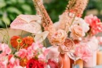 a colorful cluster wedding centerpiece with bright matte vases, pink, orange and red blooms and greenery