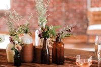 a cool relaxed cluster wedding centerpiece of apothecary bottles and vases, with greenery and wildflowers