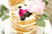 a delicious waffle wedding cake with blackberries, cream and a large pink peony on top