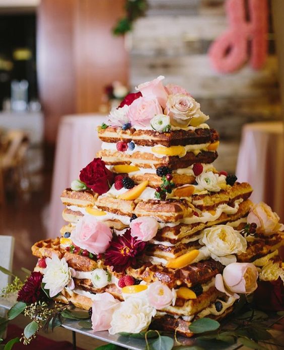 a large square waffle wedding cake with cream, fresh peaches and blusha nd red flowers is adorable
