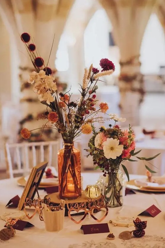 a lovely cluster fall wedding centerpiece of white, orange and red and burgundy blooms, both fresh and dried, some candles and hearts