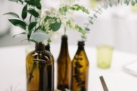 a lovely cluster wedding centerpiece of bottles with greenery and some white blooms is a pretty modern rustic decor idea