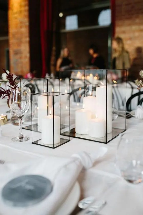 a modern and classy wedding centerpiece of glass candle lanterns with pillar candles and some candles aorund is cool