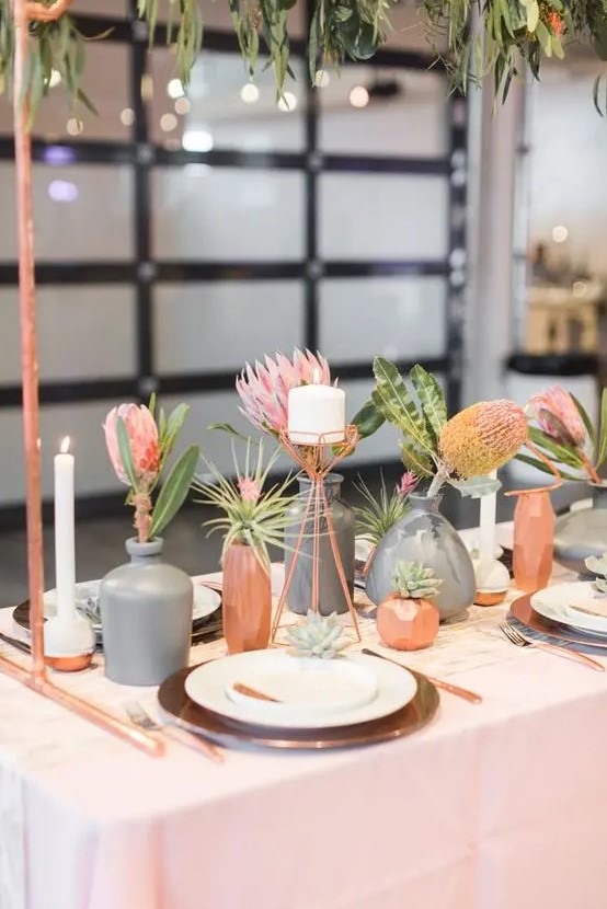 a modern cluster wedding centerpiece with copper and grey vases, bold pink blooms and greenery and candles