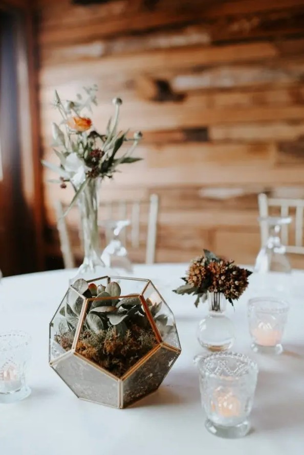 a modern fall wedding centerpiece of a terrarium with succulents, dried blooms and leaves, a rust flower and greenery in a vase
