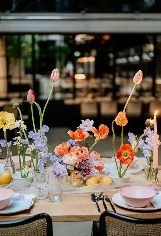 a multi-color cluster wedding centerpiece of orange, red and yellow poppies, orange tulips and ranunculus, lilac flowers