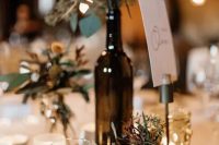 a pretty eclectic wedding centerpiece of a wood slice, candleholders, a bottle with greenery, small vases with greenery is cool