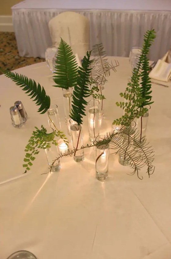 a relaxed cluster wedding centerpiece of matching glasses and various types of greenery and fern is amazing