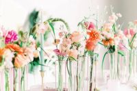 a romantic modern secret garden wedding centerpiece of sheer vases with super bright blooms and some greenery and colorful candles