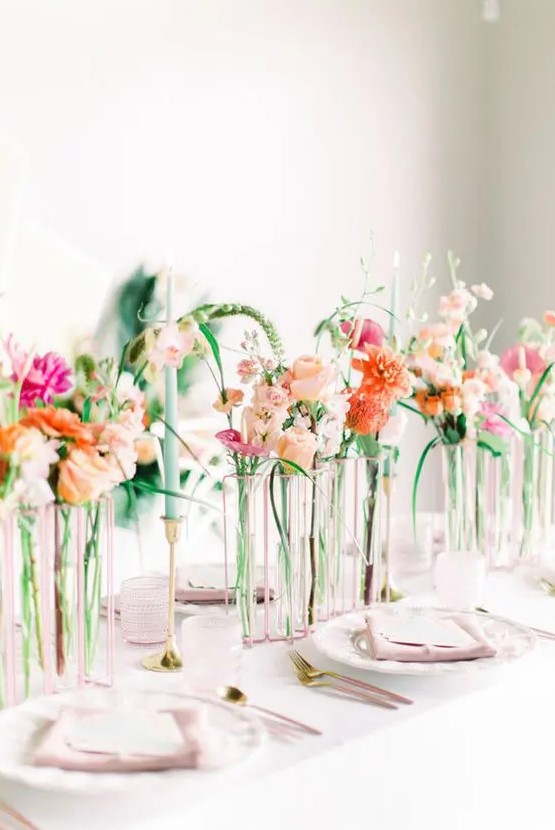 a romantic modern secret garden wedding centerpiece of sheer vases with super bright blooms and some greenery and colorful candles