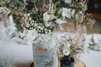a rustic wedding centerpiece of a wood slice, bottles with white blooms, thistles and greenery and a single candle is wow