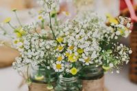 a rustic wedding centerpiece of a wood slice, jars wrapped with twine, daisies and baby’s breath is a very cozy idea