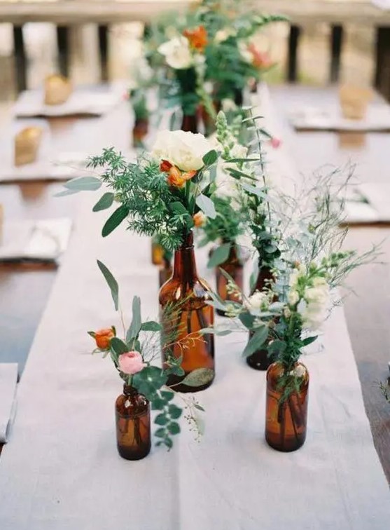 a simple cluster weddng centerpiece of dark bottles and greenery and neutral and pastel blooms is super chic