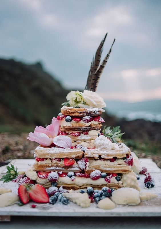 a square waffle wedding cake with whipped cream, dresh berries and blooms and feathers for a summer wedding