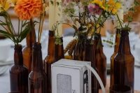 an eclectic wedding centerpiece of beer bottles with bright blooms and greenery, tall and thin candles and a white music player