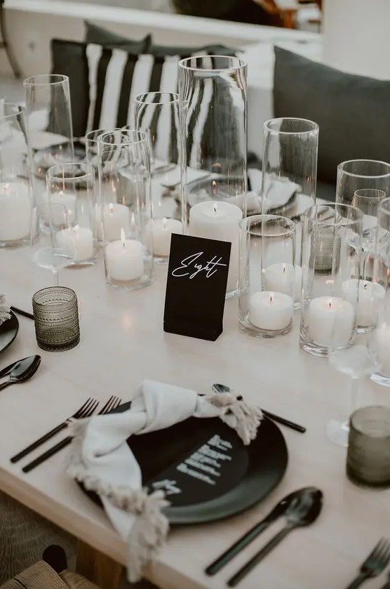 an elegant modern wedding tablescape with pillar candles, black plates and cutlery, black glasses and a card is chic