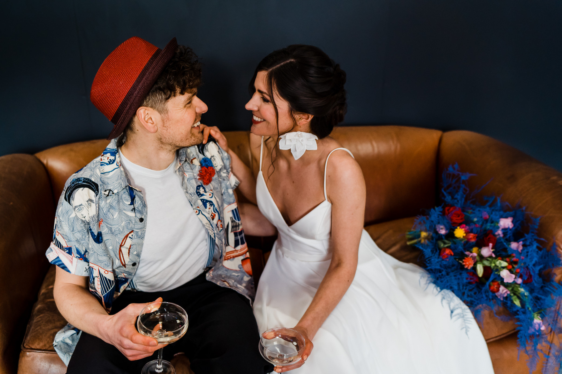The groom was wearing black pants, a colorful printed shirt, a white tee and a red hat