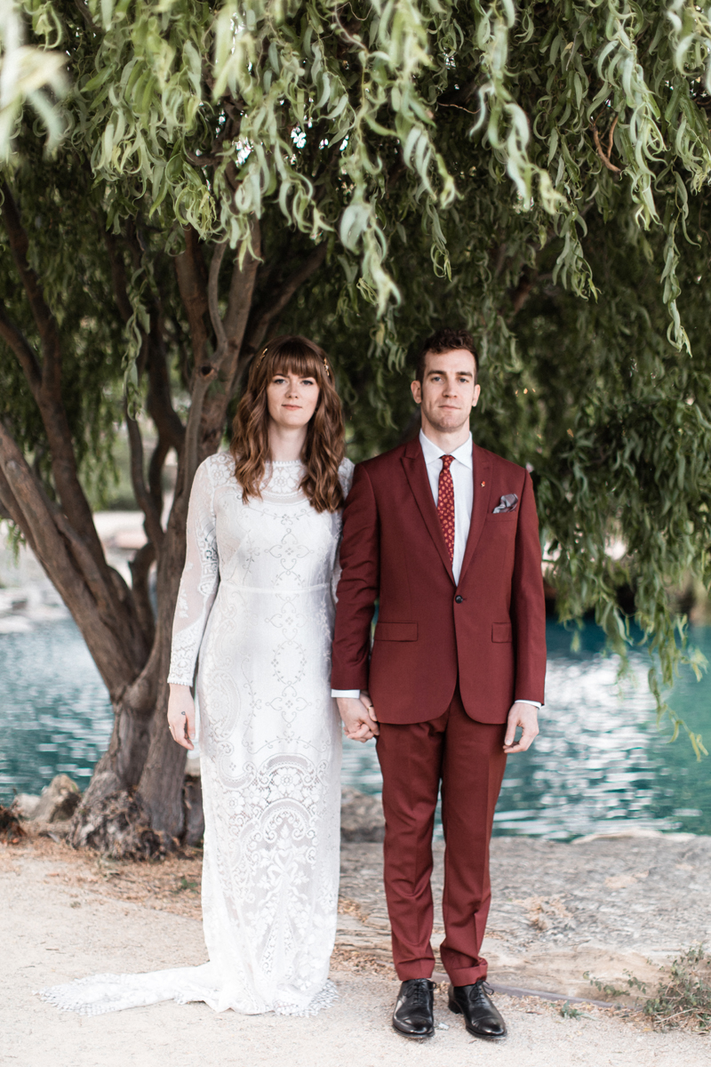 The bride was wearing a chic lace sheath wedding dress with long sleeves, a high neckline and a train and the groom was wearing a burgundy suit with a red printed tie