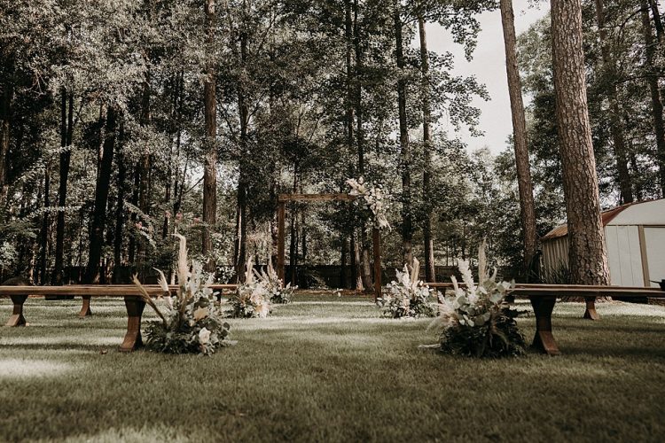 The wedding ceremony space was done with wooden benches and an arch, with blush blooms, greenery and pampas grass