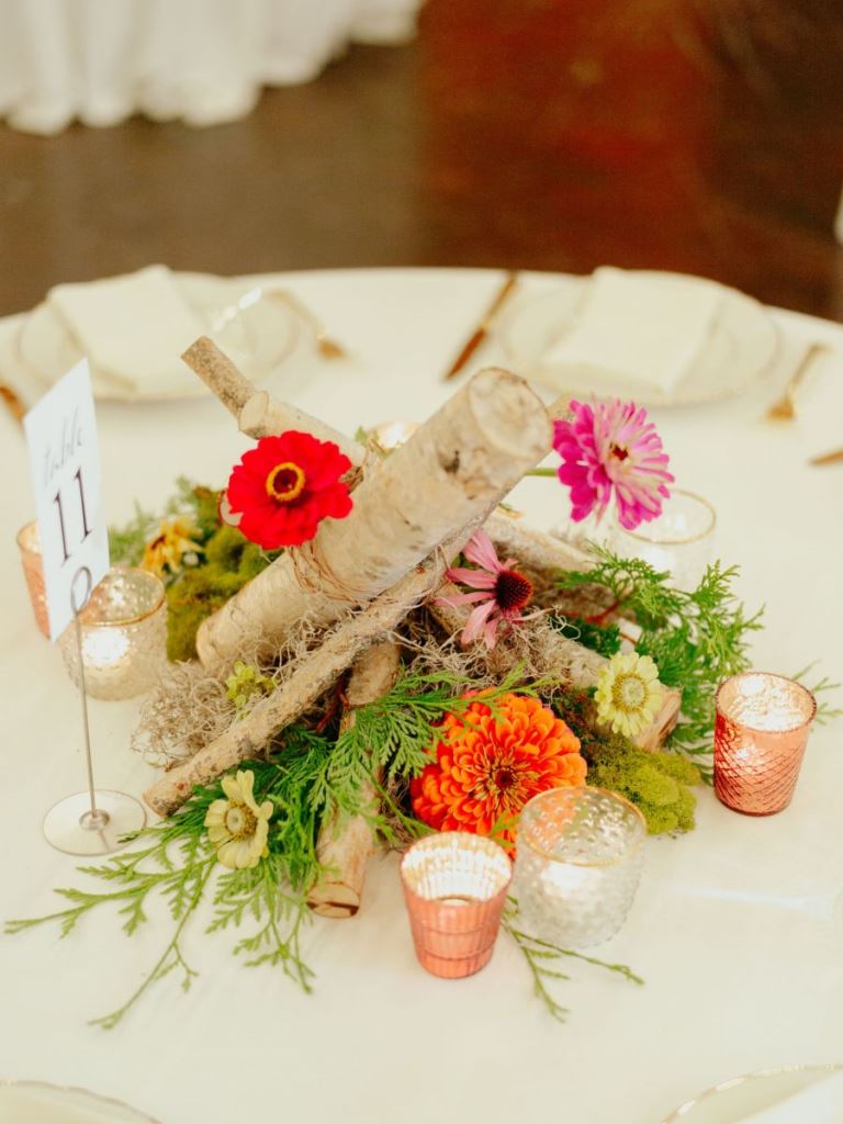 The wedding centerpiece was done with bright blooms, greenery and firewood and candles around