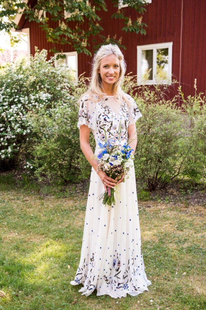 a charming A-line wedding dress with pastel and white floral embroidery all over the gown and a matching blue bouquet