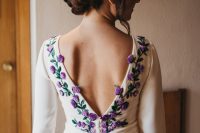 a wedding dress featuring purple and lilac embroidered flowers and leaves, a cutout back on buttons and a long train