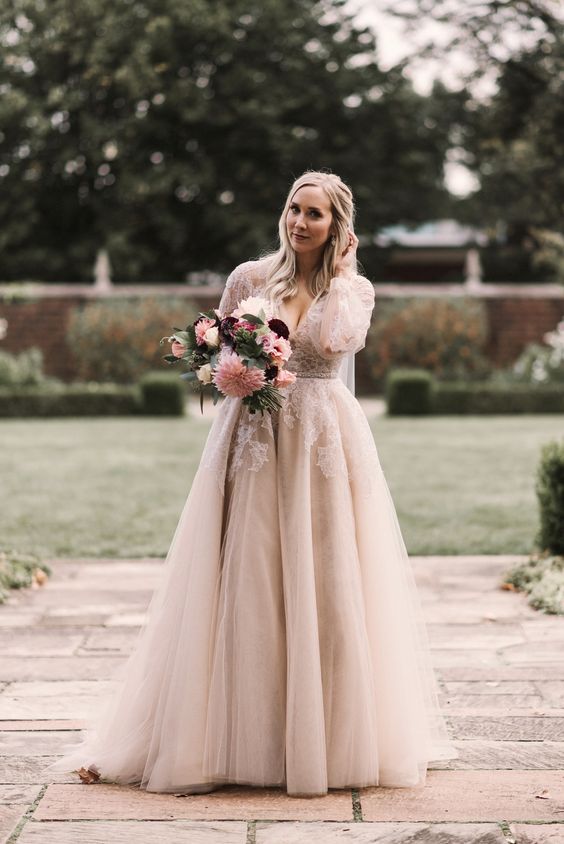 a blush and white A-line wedding dress with a deep neckline, long sleeves is a very romantic piece for a fairy-tale bride