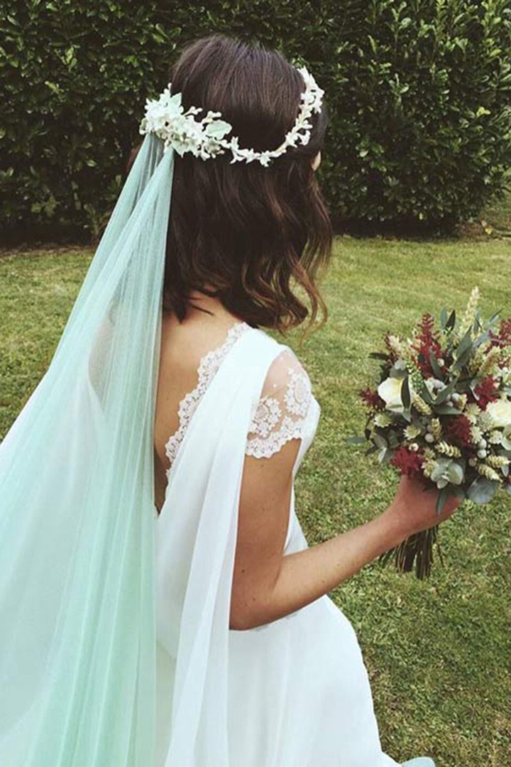 a beautiful lace A-line wedding dress with a cape, a floral crown and a light blue veil for a 'something blue' touch