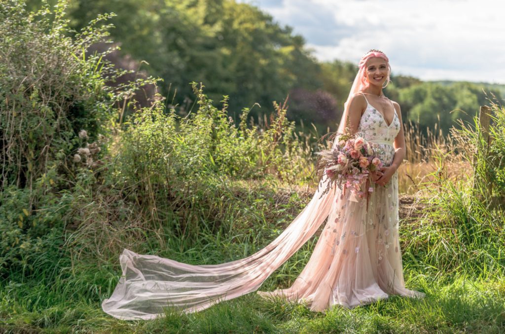 a blush floral applique wedding dress with a V neckline and a train, a blush veil and pink hair for a pastel bridal look