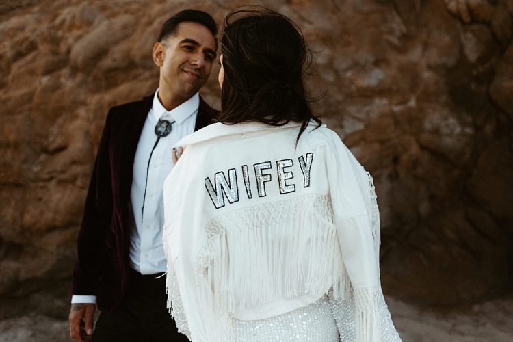 The bride covered up with a white jacket with tassels, macrame and sequin letters