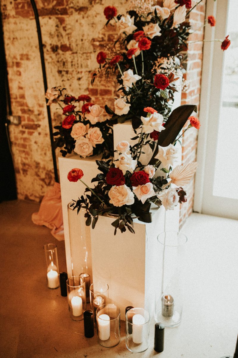 A wedding altar in white, with white and red blooms and black and white candles