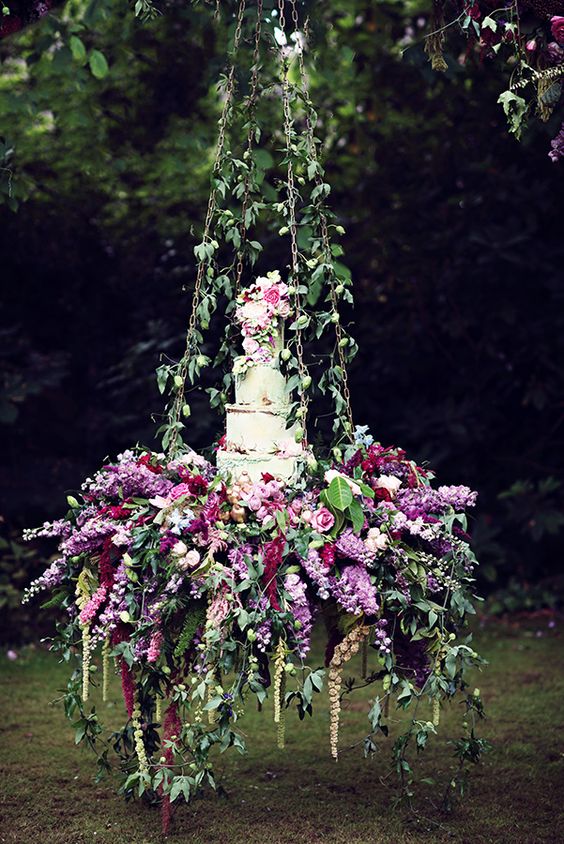 serve your wedding cake on a hanging piece with greenery, purple and pink blooms and top it with the same flowers