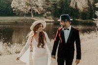 a burgundy velvet tux with black lapels, black pants and shoes, a navy hat and a bow tie for a refined boho look