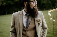 a winter boho groom wearing black jeans, a creamy plaid blazer, a matching brown waistcoat, a white shirt, a grey tie and a black hat