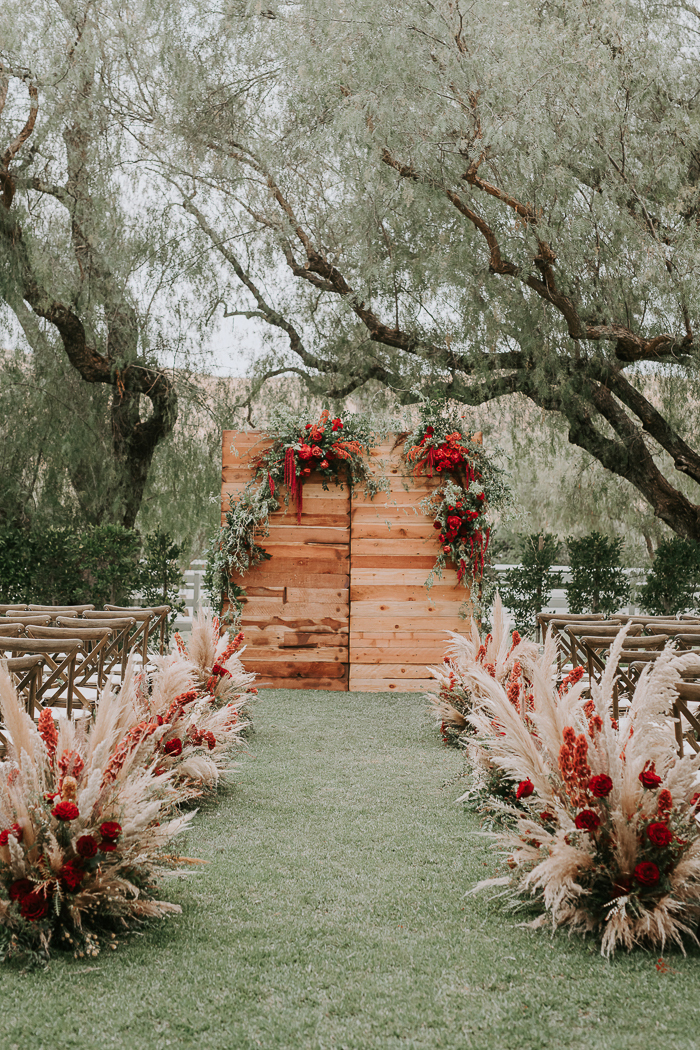 The wedding ceremony space was done with greenery, red blooms and pampas grass around