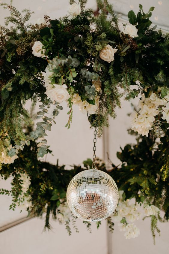 a greenery, fir, white rose wedding chandelier with a hanging disco ball is a unique idea for wedding decor