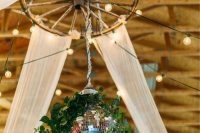 08 a rustic wedding chandelier of an old wheel, lights, some sheer fabric and a disco ball decorated with greenery