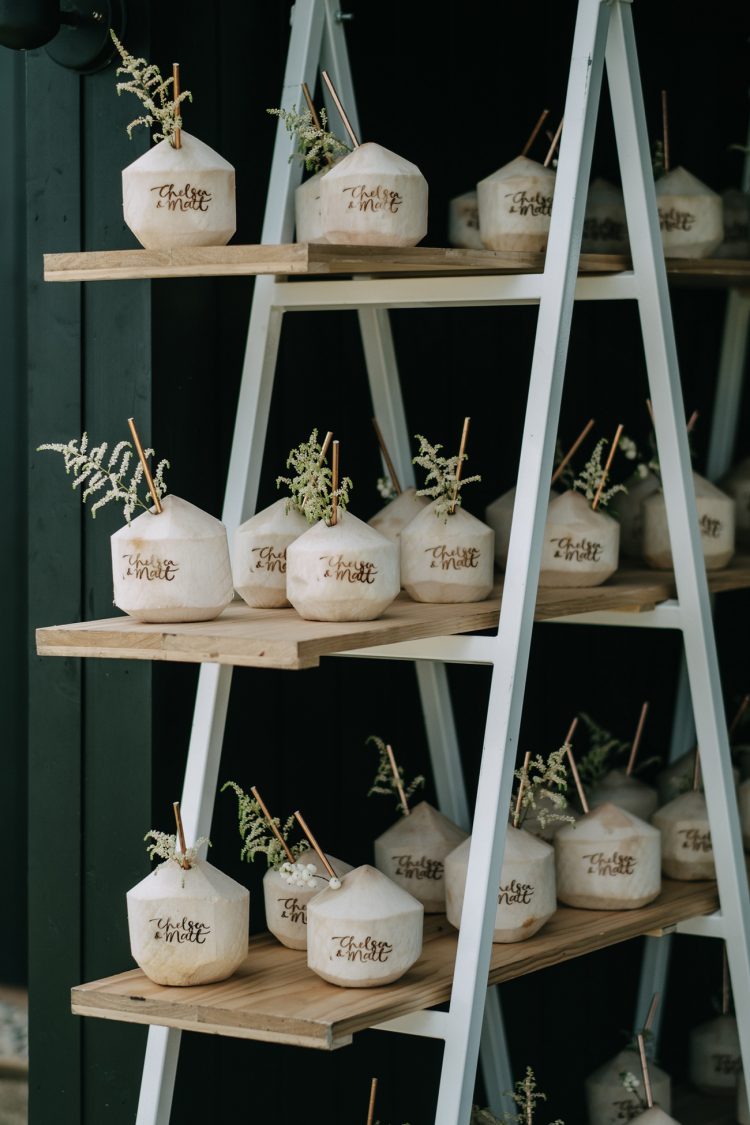 a stand with drinkable coconuts, metal straws and greenery is a great idea for a tropical wedding
