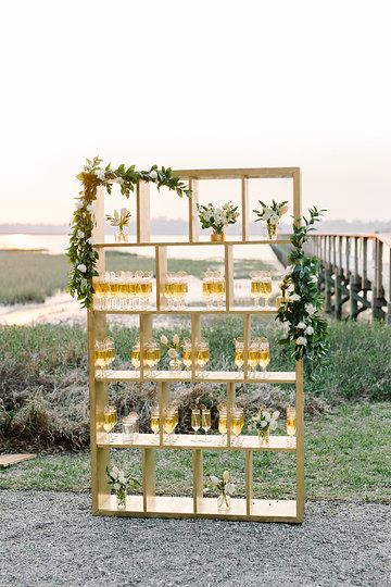 a tall wooden stand with lots of shelves, greenery and neutral blooms and drinks in glasses