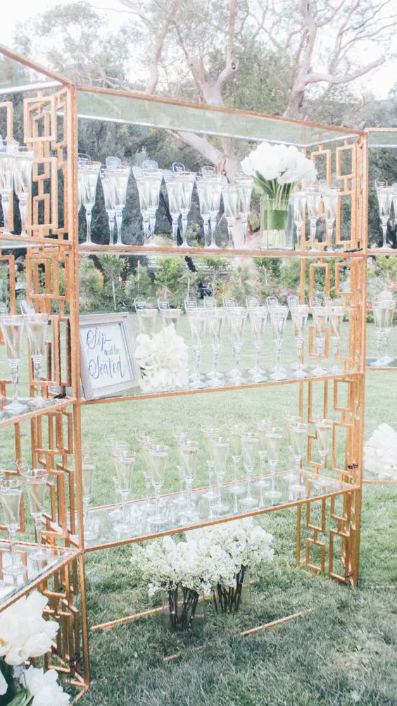 a glam metallic stand with glass shelves, white florals and glasses is a refined way to serve drinks