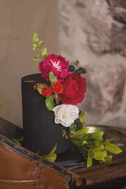Bride and groom chose a black one tier cake decorated with red, white and pink roses, a greenery and blackberries