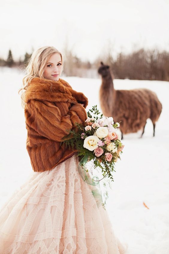 a blush wedding dress paired with a brown faux fur jacket create a lovely and chic look with a soft touch of color