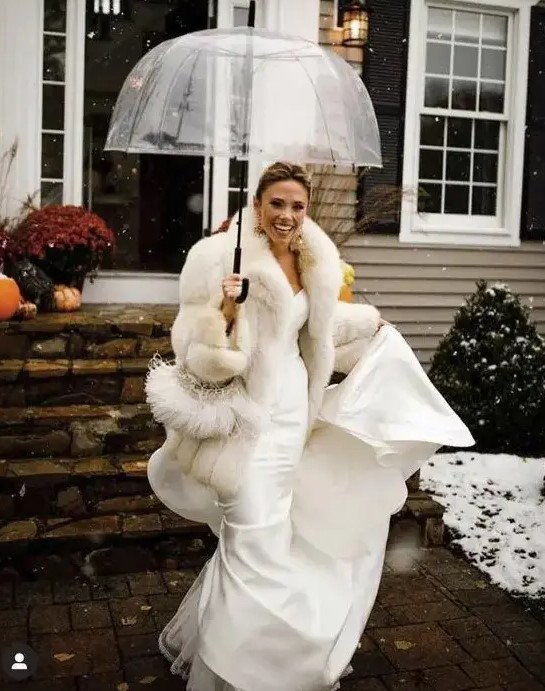 a glam bridal outfit with a strapless mermaid wedding dress, a white faux fur coat and statement earrings for a winter celebration