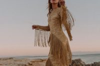 a gold lace sheath wedding dress with a high neckline, long sleeves and long fringe on the dress and sleeves
