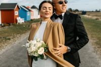 a modern plain wedding dress with a thigh high slit and a beige coat to keep the bride warm and stylish