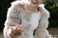 a modern winter bridal look with a plain fitting wedding dress and a neutral faux fur coat is cool and fresh