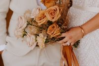 a refined ombre rose wedding bouquet from blush and rust-colored blooms, dried herbs and rust-colored ribbons