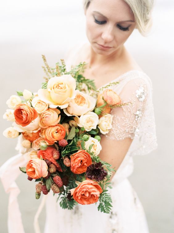 a refined ombre wedding bouquet from peachy to red and orange blooms, with greenery and berries for a fall bride